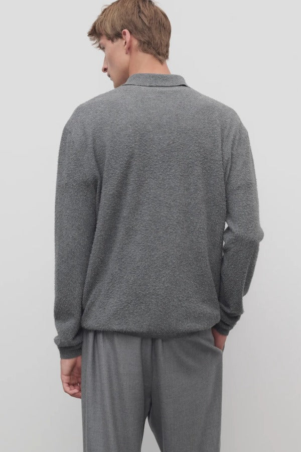 Back view of grey melange almot sweater on model wearing grey pants, against a white background.