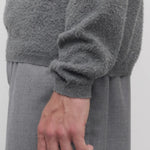 Side closeup view of grey melange almot sweater on model wearing grey pants, against a white background.