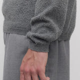 Side closeup view of grey melange almot sweater on model wearing grey pants, against a white background.