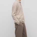 Side view of beige melange almot sweater on model wearing khaki pants against a white background.