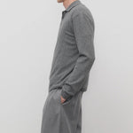 Side view of grey melange almot sweater on model wearing grey pants, against a white background.
