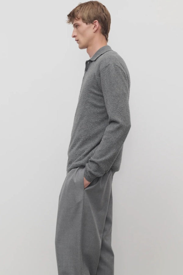 Side view of grey melange almot sweater on model wearing grey pants, against a white background.