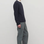 Side view of grey men's fred pants on model wearing black sweater and boots, against a white background.