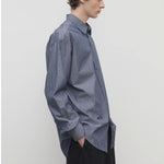 Side view of blue/white men's miller stripe shirt on model wearing black trousers, against a white background.