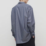 Back view of blue/white men's miller stripe shirt on model wearing black trousers, against a white background.