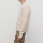 Side view of ecru nikola sweater on model wearing khakis against a white background.