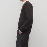 Side view of brown  melange men's rod sweater on model wearing grey trousers, against a white background.