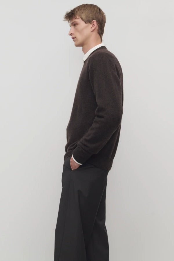Side view of brown  melange men's rod sweater on model wearing grey trousers, against a white background.