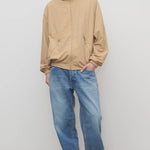 Front view of medium blue men's ross jean on model wearing sand windbreaker and sneakers, against a white background.