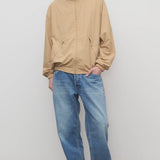 Front view of medium blue men's ross jean on model wearing sand windbreaker and sneakers, against a white background.