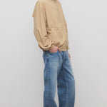 Side view of medium blue men's ross jean on model wearing sand windbreaker and sneakers, against a white background.