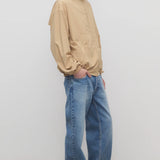 Side view of medium blue men's ross jean on model wearing sand windbreaker and sneakers, against a white background.