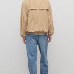 Back view of medium blue ross jean on model wearing sand windbreaker and sneakers, against a white background.