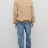 Back view of medium blue ross jean on model wearing sand windbreaker and sneakers, against a white background.