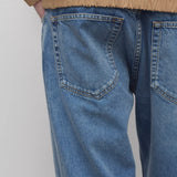 Back closeup view of medium blue ross jean on model wearing sand windbreaker, against a white background.