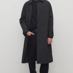 Front view of black tarian coat on model wearing black pants, shirt and boots, against a white background.