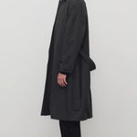 Side view of black tarian coat on model wearing black pants, shirt and boots, against a white background.