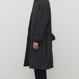Side view of black tarian coat on model wearing black pants, shirt and boots, against a white background.