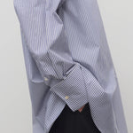Side closeup view of white and blue shirt on model wearing black trousers, against a white background.