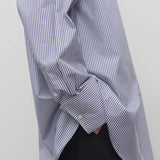 Side closeup view of white and blue shirt on model wearing black trousers, against a white background.