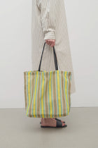 Front view of mesh and leather bag on white background, with model wearing light silk dress and sandals. 