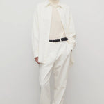 Front view of white neriah pant on model wearing ivory top, white jacket and sneakers, against a white background.
