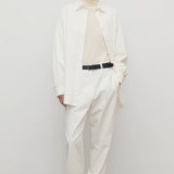Front view of white neriah pant on model wearing ivory top, white jacket and sneakers, against a white background.