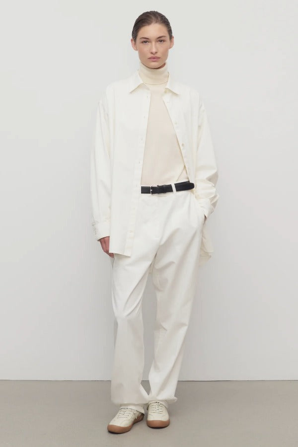 Front view of white neriah pant on model wearing ivory top, white jacket and sneakers, against a white background.