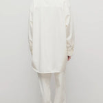 Back view of white neriah pants on model wearing white jacket and sneakers, against a white background.