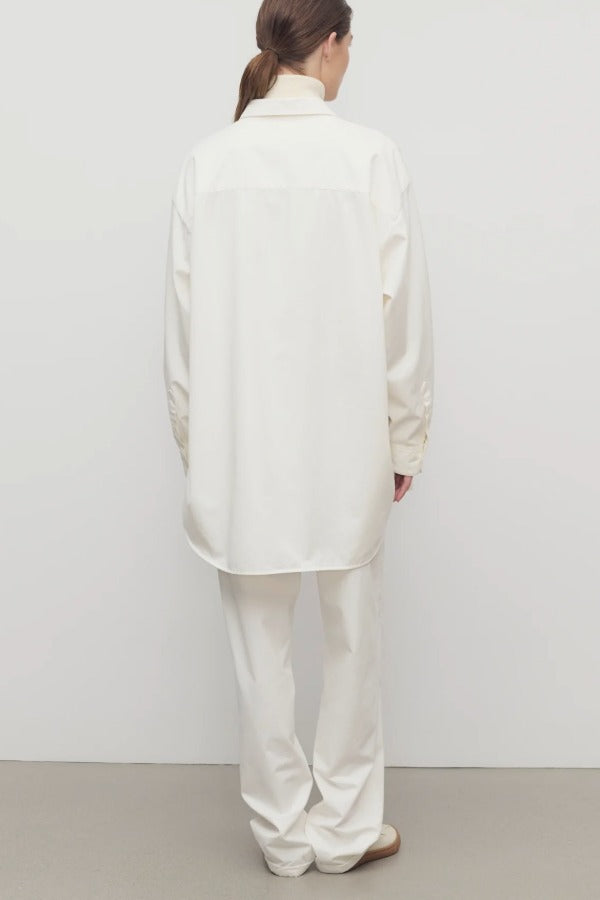 Back view of white neriah pants on model wearing white jacket and sneakers, against a white background.