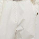 Front closeup of white neriah pants on model wearing ivory top and black belt, against a white background.
