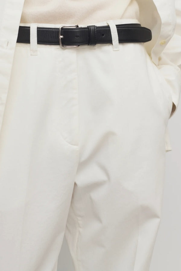 Front closeup of white neriah pants on model wearing ivory top and black belt, against a white background.