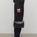 Front view of black nuance bag on model wearing black top, pants and mules, against a white background.