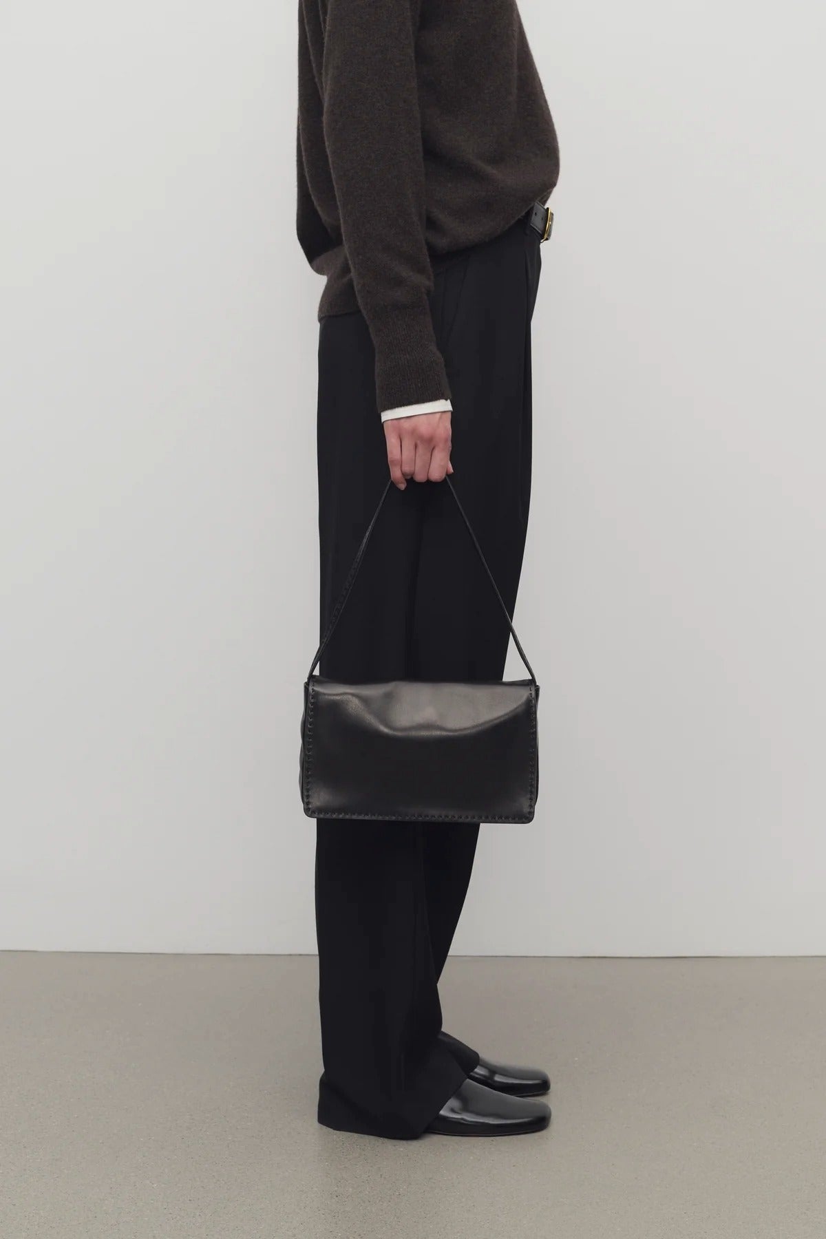 Front view of black nuance bag on model wearing black top, pants and mules, against a white background.