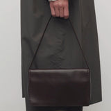 Front view of dark brown nuance bag on model wearing grey trench coat and khaki pants, against a white background.