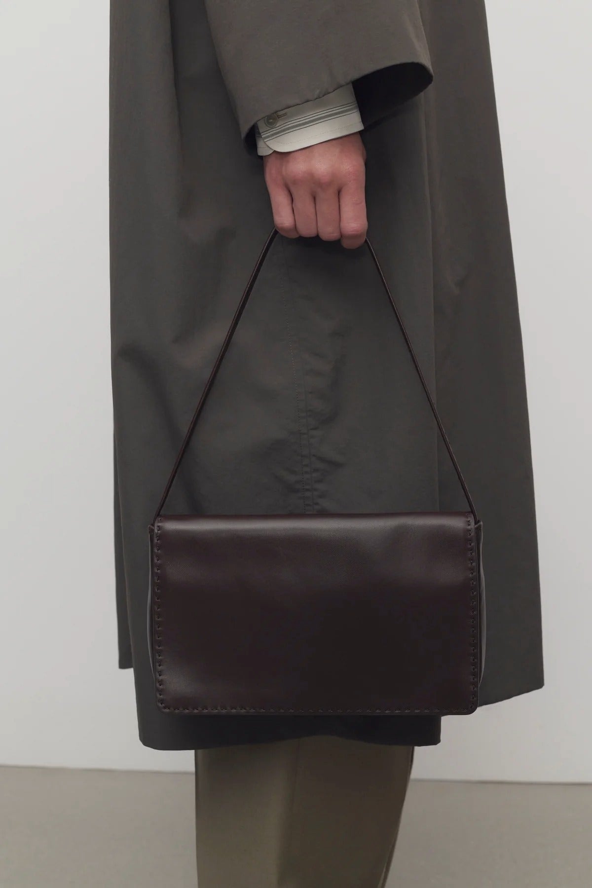 Front view of dark brown nuance bag on model wearing grey trench coat and khaki pants, against a white background.