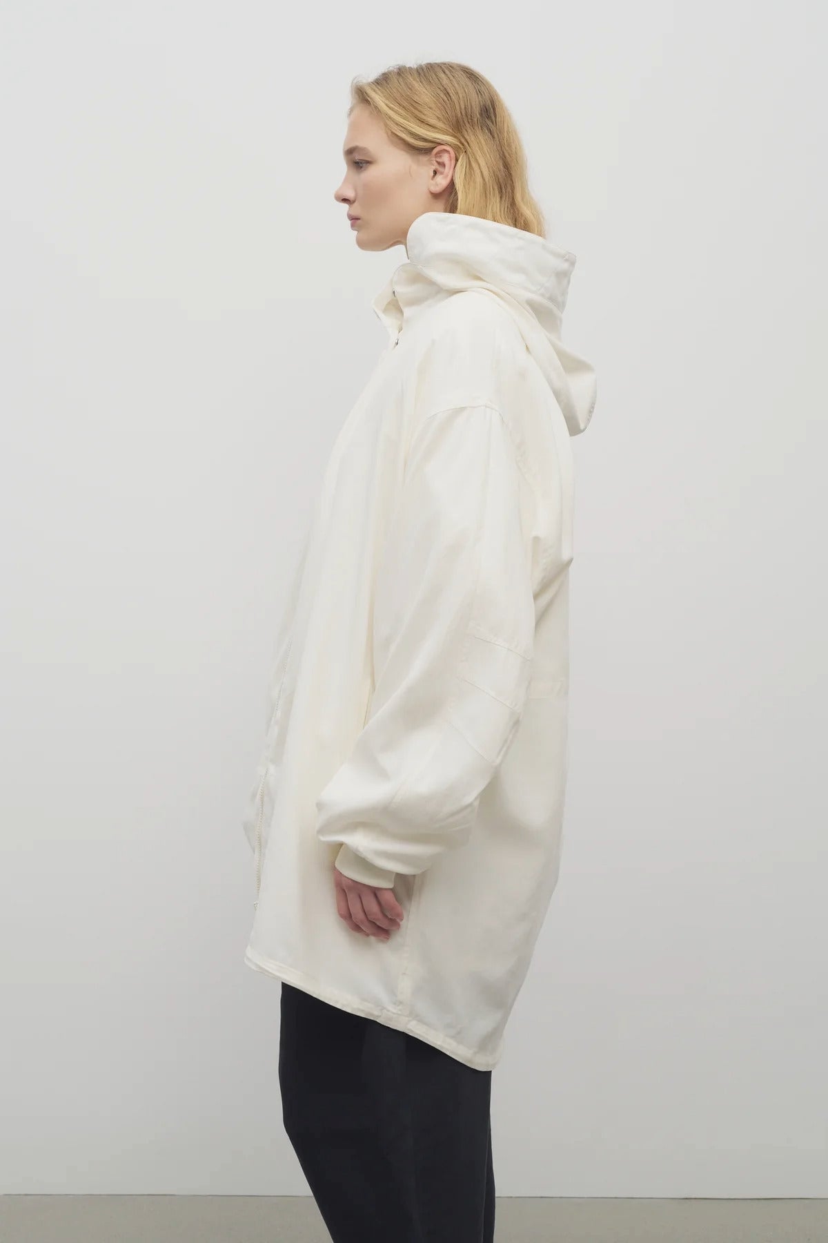 Side view of off-white Kemetina Coat on model wearing black trousers, against white background.