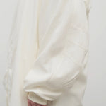 Side closeup view of off white Kemetina coat on model wearing black trousers, against white background.