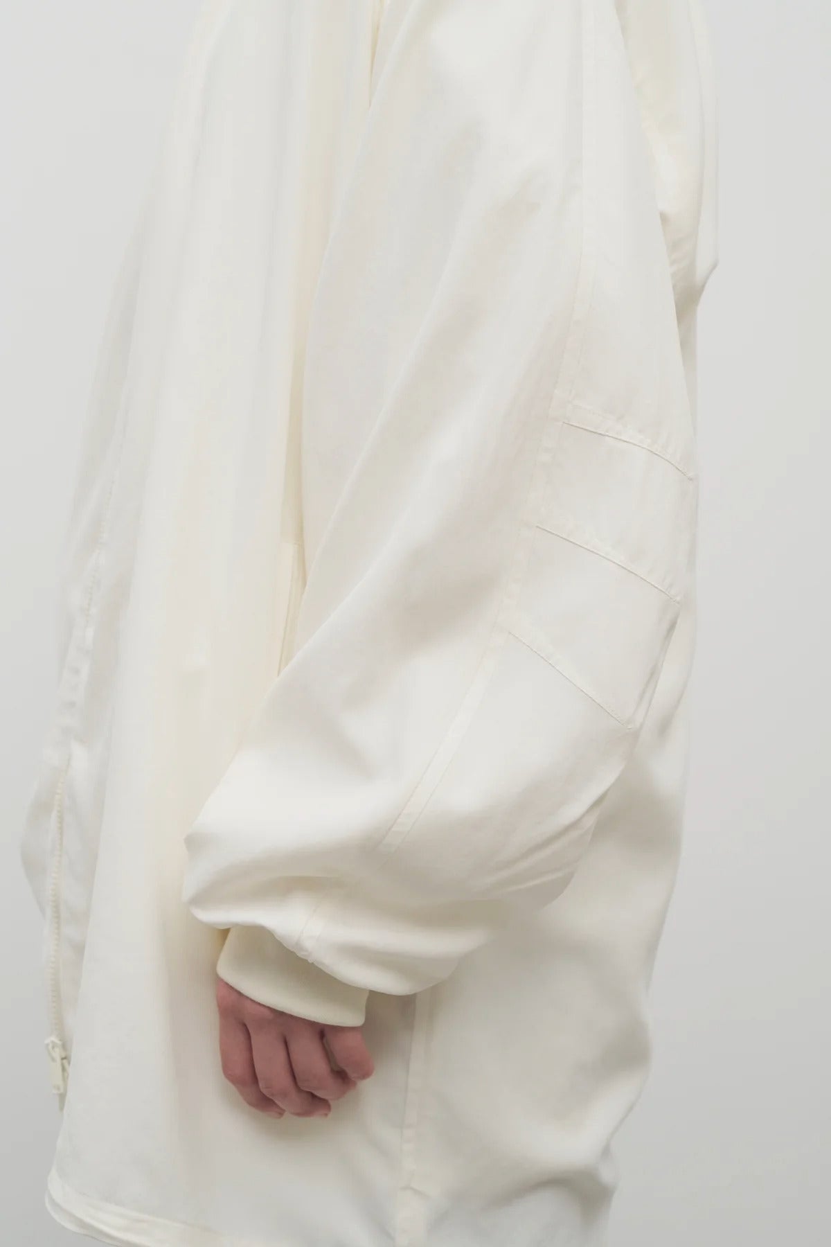 Side closeup view of off white Kemetina coat on model wearing black trousers, against white background.