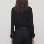 Back view of black petra shirt on model wearing black trousers, against a white background.