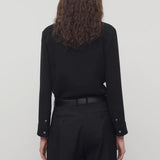 Back view of black petra shirt on model wearing black trousers, against a white background.