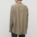 Back view of military beige pino shirt on model wearing grey pants, against a white background.