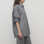Side view of grey pino shirt on model wearing grey pants, against a white background.