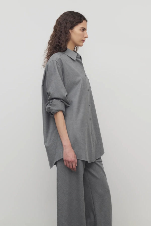 Side view of grey pino shirt on model wearing grey pants, against a white background.
