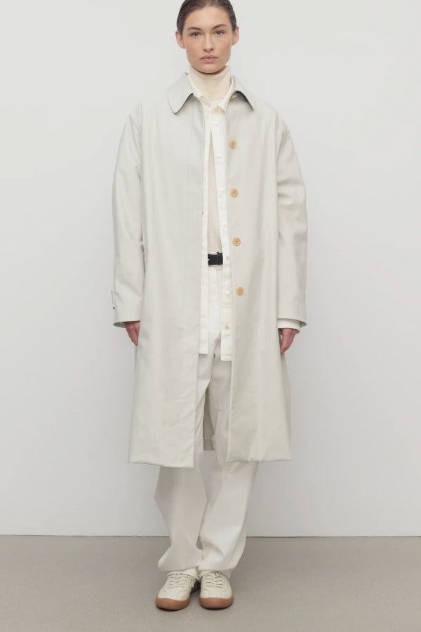 Front view of snow pluma coat on model wearing white top, pants and sneakers, against a white background.