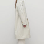 Side view of snow pluma coat on model wearing white top, pants and sneakers, against a white background.