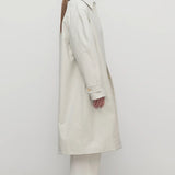 Side view of snow pluma coat on model wearing white top, pants and sneakers, against a white background.