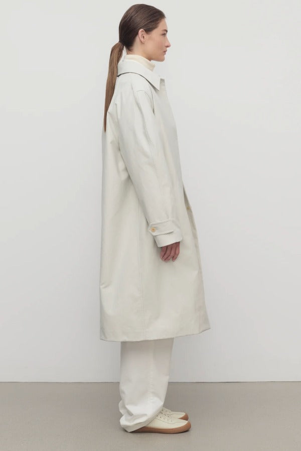 Side view of snow pluma coat on model wearing white top, pants and sneakers, against a white background.