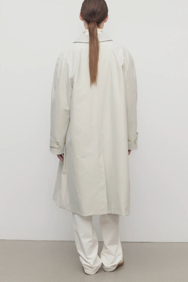 Back view of snow pluma coat on model wearing white pants and sneakers, against a white background.