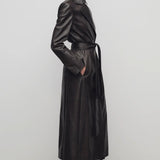 Side view of coffee raisa coat on model wearing low heels, against a white background.